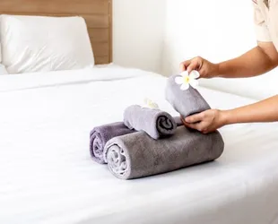 Hands of hotel maid putting plumeria flower and towels on the bed in the luxury hotel room ready for tourist travel.